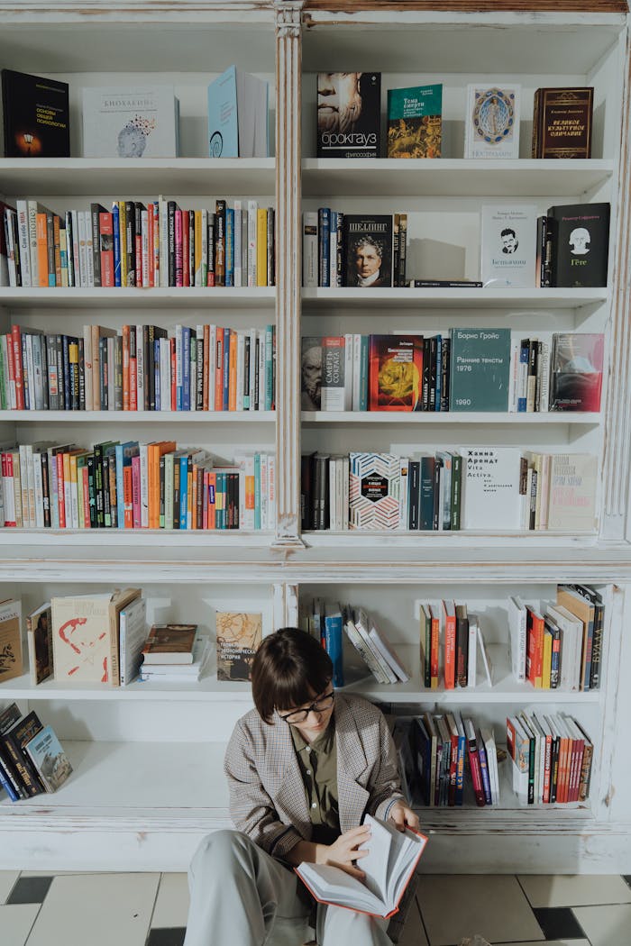 why-choose-us Woman reading a book in a modern library setting, surrounded by diverse literature.